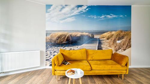 a yellow couch in a room with a painting of a pier at Apartamenty PIAMOLA Bursztynowe Osiedle Jantar in Jantar
