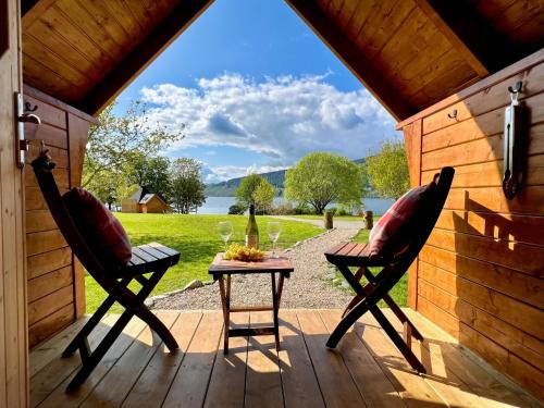 um alpendre com 2 cadeiras e uma mesa com copos de vinho em Seal Cove Cabin - Luxury Glamping em Cairndow