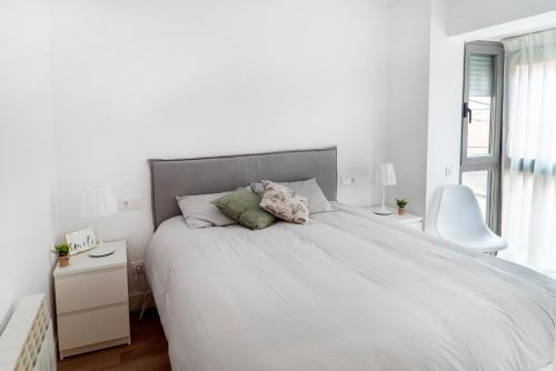 a white bedroom with a large bed and a white chair at Preciosos apartamentos Riojaland en Lardero in Lardero