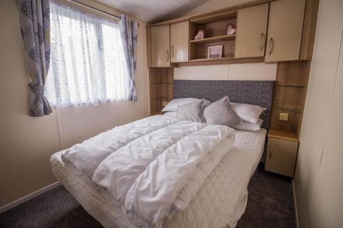 a bedroom with a bed with white sheets and a window at 8 Berth Caravan For Hire Near Clacton-on-sea In Essex Ref 26287e in Clacton-on-Sea