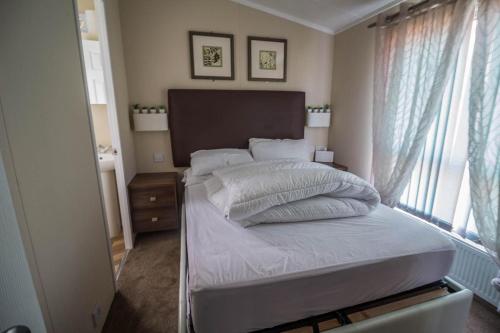 a bedroom with a bed with white sheets and a window at Beautiful Caravan At Highfield Grange Holiday Park In Essex Ref 26687p in Clacton-on-Sea