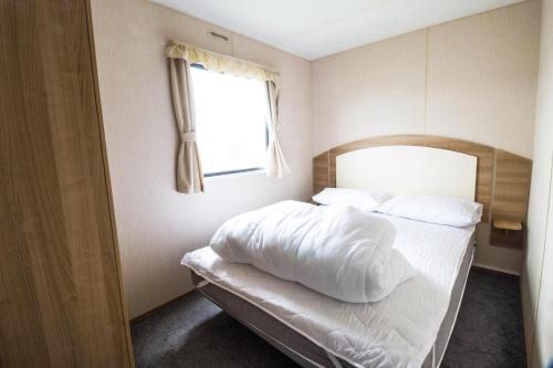 a bedroom with a bed with white sheets and a window at 8 Berth Caravan At Highfield Grange In Essex Ref 26267e in Clacton-on-Sea
