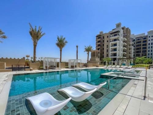 a swimming pool with white chairs and some buildings at Vogue Vacation Homes, Madinat Jumeirah Living Rahaal Near Burj Al Arab One Bedroom Apartment with Balcony and Vibrant Community View, Access to all Amenities in Dubai