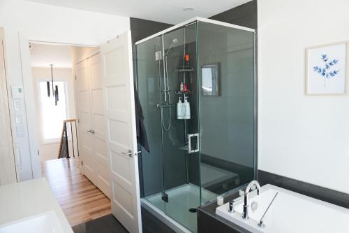 La salle de bains est pourvue d'une douche en verre et d'une baignoire. dans l'établissement Le Citadin - Maison neuve moderne & ensoleillée, à Québec