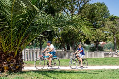 two men riding bikes on a path in a park at Camping Le Camp Du Domaine in Bormes-les-Mimosas