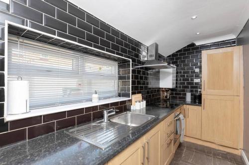 a kitchen with a sink and a black tiled wall at Large Parade Coastal House in Hartlepool