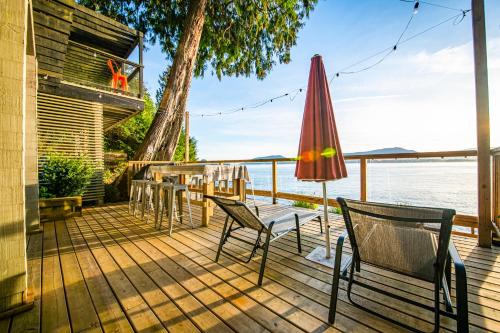 a deck with chairs and an umbrella and the water at SALT COTTAGE Waterfront Guest House with Superb Views in West Vancouver