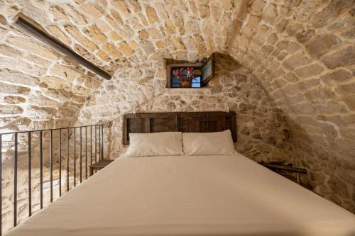 Posto letto in camera con parete in pietra. di Case-grotte degli Avi, esperienza abitativa in grotta a Modica