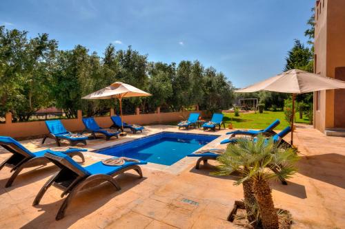 a swimming pool with blue chairs and umbrellas at Taj Atlas Wellness Boutique Hôtel & Spa in Amizmiz