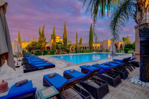 - une piscine avec des chaises longues bleues et des palmiers dans l'établissement Taj Atlas Wellness Boutique Hôtel & Spa, à Amizmiz