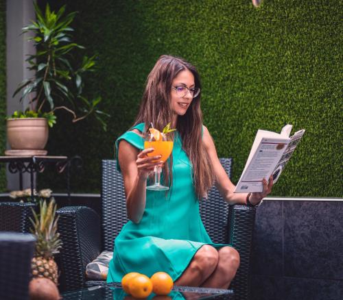una mujer sentada en una silla con una bebida y una revista en Business Hotel Plovdiv, en Plovdiv