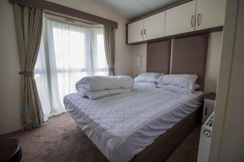 Schlafzimmer mit einem Bett mit weißer Bettwäsche und einem Fenster in der Unterkunft Modern 6 Berth Caravan At Highfield Grange In Essex Ref 26609p in Clacton-on-Sea