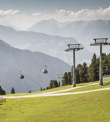 a gondola flying over a green field with mountains at Pension Alpina in Roppen
