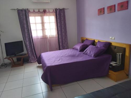 sypialnia z fioletowym łóżkiem i telewizorem w obiekcie MC Location w mieście Abidżan