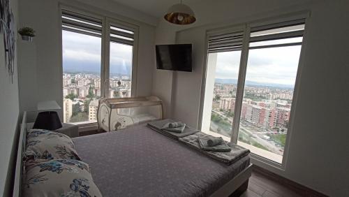 a bedroom with a bed and two large windows at 18th Floor Secure Luxury Condo With Pool & Fitness Included In Price in Skopje