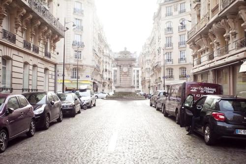 una calle de la ciudad con coches aparcados y un gran edificio en Bien situe en París