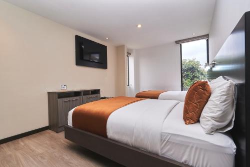 a bedroom with two beds and a tv on the wall at Hotel & Suites en Cuenca, Venue Batán in Cuenca