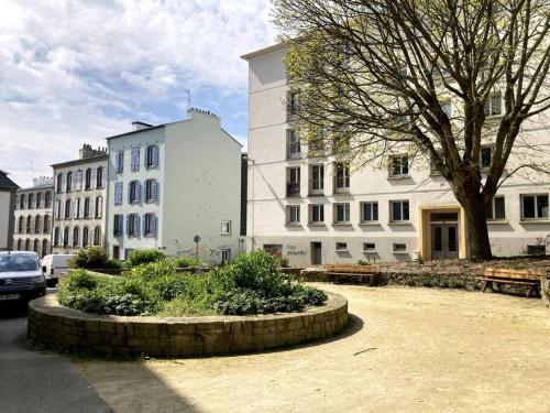 un groupe de bâtiments blancs avec un arbre et des bancs dans l'établissement Les Capucins.Appartement élégant,Vue sur le jardin, à Brest