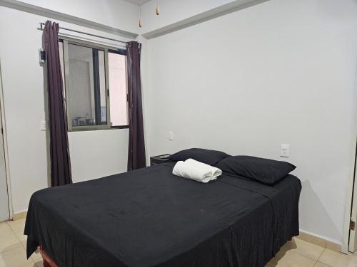 a bedroom with a bed with a black blanket and a window at El Padrino in Akumal