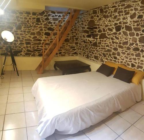 - un lit blanc dans une chambre dotée d'un mur en pierre dans l'établissement Maison charmante avec jardin centre-ville proche puy du fouu Arrivée autonome, à Cholet