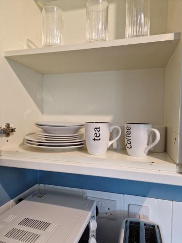 zwei Kaffeetassen auf einem Regal mit Tellern in der Unterkunft Chique Maidstone Studio II in Kent
