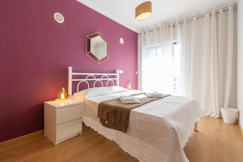 een slaapkamer met een wit bed en een paarse muur bij Apartamento Mãe Soberana in Loulé