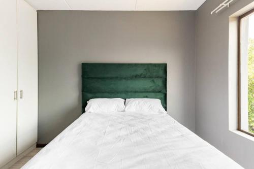 a white bed in a room with a green headboard at 2 bedroom apartment close to OR Tambo in Kempton Park