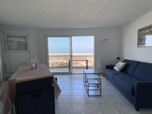 un salon avec un canapé bleu et une table dans l'établissement Appartement RDC face à la mer avec balcon et parking privatif - FR-1-672-26, à Merlimont