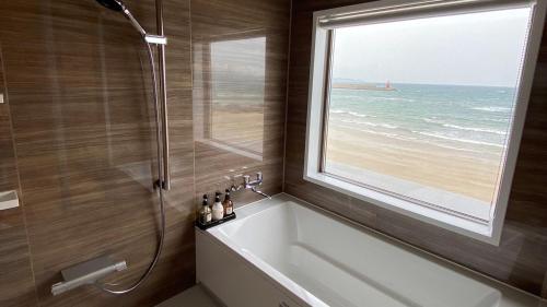 a bathroom with a tub and a window and the ocean at Genkai Ryokan in Munakata