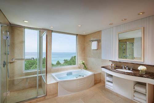 a bathroom with a tub and a shower and a window at The Shilla Jeju in Seogwipo