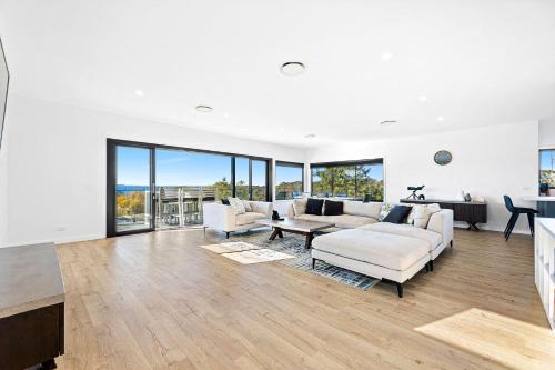 Montague Sunrise 2 Riley Street Narooma في ناروما: غرفة معيشة بأثاث أبيض ونوافذ كبيرة