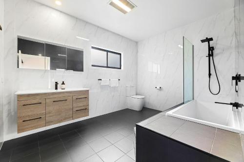 Montague Sunrise 2 Riley Street Narooma في ناروما: حمام مع حوض استحمام ومرحاض ومغسلة