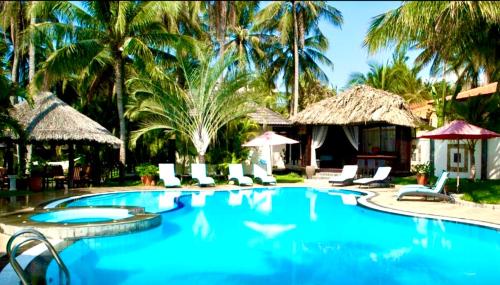 a pool at a resort with chairs and palm trees at Jaguar House Resort Muine in Mui Ne