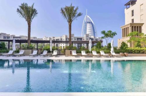 a pool with chairs and palm trees and a building at Madinat Jumeirah Living, MJL Dubai in Dubai