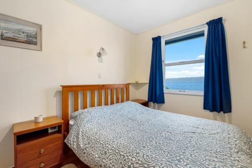 a bedroom with a bed and a window with blue curtains at The Blue Bach - Lake Rotoiti Holiday Home in Rotoiti