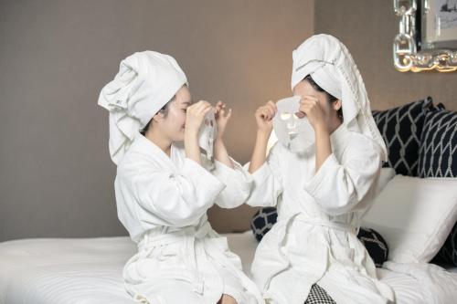 two women sitting on a bed drinking from cups at Kent Hotel Gwangalli by Kensington in Busan