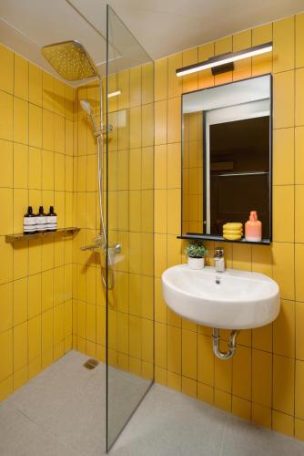 a yellow tiled bathroom with a sink and a shower at lyf Malate Manila managed by The Ascott Limited in Manila