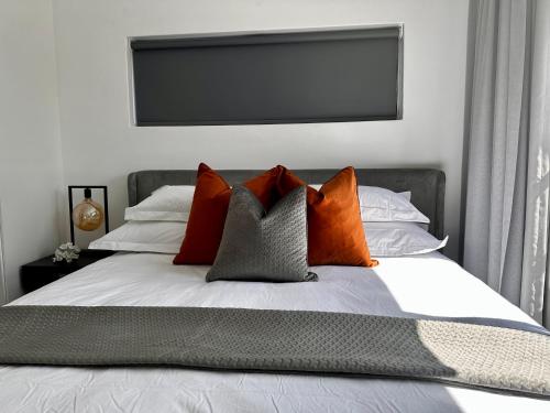 Una cama con almohadas de color naranja y gris. en Stylish Executive Apartment with Power Backup, en Johannesburgo