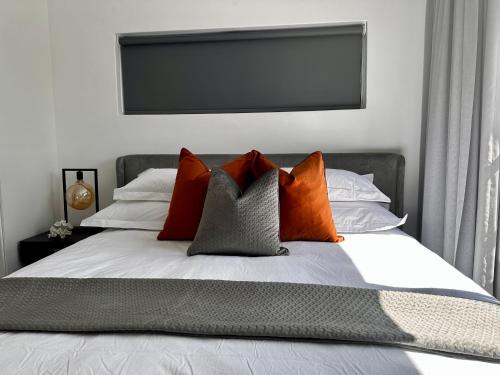 a bed with orange and grey pillows on it at Stylish Executive Apartment with Power Backup in Johannesburg