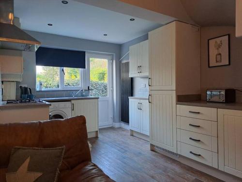 una cocina con armarios blancos y un sofá en una habitación en Cosy cottage near Alton Towers, en Rocester