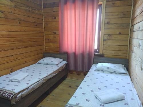 two beds in a room with wooden walls and a window at Пансионат Сабрина in Bosteri