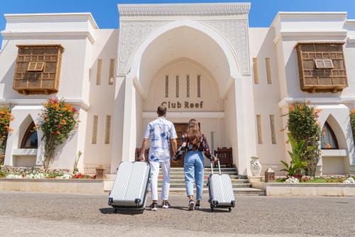 Club Reef Resort & Spa في شرم الشيخ: رجل وامرأة يسيران بأمتعتهم أمام مبنى