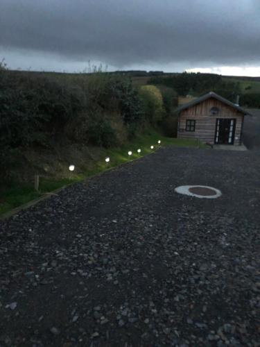 un camino de grava con un edificio y luces en él en Bryn Fach Log Cabin en Merthyr Cynog