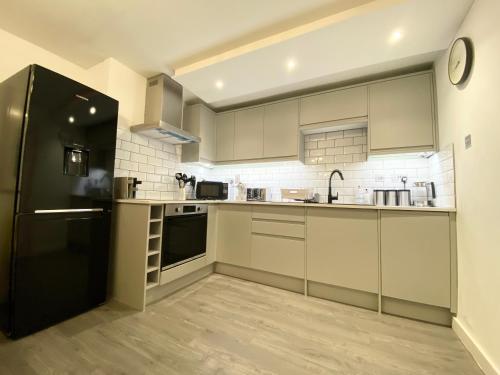 a kitchen with a black refrigerator and white cabinets at "The Garden Apartment Newquay" by Greenstay Serviced Accommodation - Beautiful 2 Bed Apartment With Parking & Outside Terrace, Close To Beaches, Shops & Restaurants -Perfect For Families, Couples, Small Groups & Business Travellers in Newquay