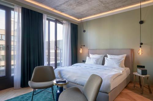 a bedroom with a bed and two chairs and windows at Gekko House Frankfurt, a Tribute Portfolio Hotel in Frankfurt/Main