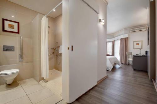 a white bathroom with a toilet and a bed at Protea Hotel by Marriott Midrand in Midrand