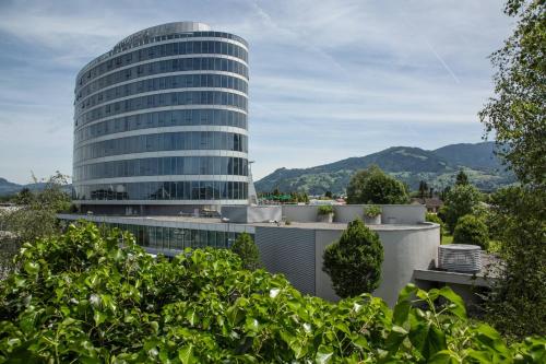 a tall glass building with mountains in the background at Four Points by Sheraton Panoramahaus Dornbirn in Dornbirn