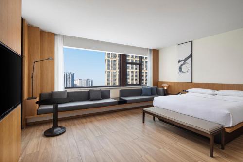 Fairfield by Marriott Hangzhou Xiaoshan في هانغتشو: غرفة نوم بسرير واريكة ونافذة