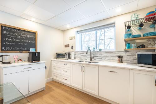 a kitchen with white cabinets and a blackboard on the wall at Escale Vélo & Spa en Estrie in Shefford