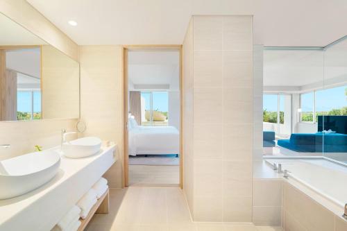 a bathroom with two sinks and a tub and a bedroom at IRAPH SUI, a Luxury Collection Hotel, Miyako Okinawa in Miyako Island
